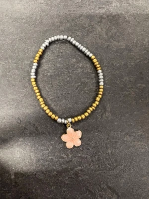 Pärlarmband med blomberlock storlek M  - Armband med pärlor i guld och silver samt en rosa blomma som hänge. 