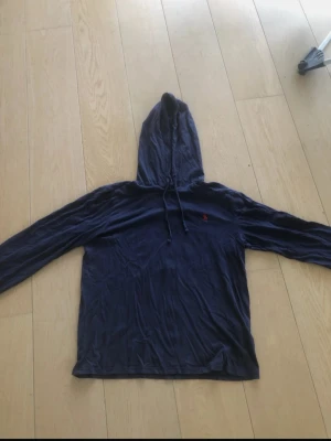 Mörkblå hoodie från Polo Ralph Lauren - Snygg mörkblå hoodie från Polo Ralph Lauren med klassisk röd logga broderad på bröstet. Hoodien har dragsko i huvan och är tillverkad i mjukt material som känns skönt mot huden. Sitter som en S