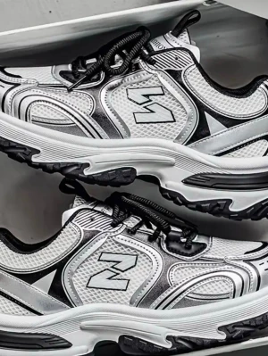 Svarta och vita sneakers med mönster - Snygga sneakers i svart och vitt med coola grafiska mönster och silvriga detaljer. Ovandelen är i mesh och syntet, med svart sula och grovt mönstrad undersida för extra grepp. Märket 'New' syns på plösen och sidan. Perfekta för en trendig streetstyle.