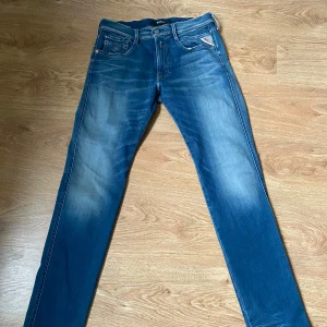 Blå Replay jeans, midwaist, storlek 32/32 - Säljer ett par snygga blå jeans från Replay i storlek 32/32. Jeansen har klassisk femficksdesign, Replay-logga vid myntfickan och snygga slitningar framtill och baktill. Modellen är rak med normal passform och tillverkad i mjukt denimtyg.