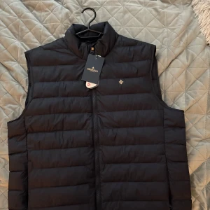 Blå dunväst från Morris XL - Snygg blå dunväst från Morris med quiltad design och hög krage. Västen är helt ny, säljer på grund av för liten eftersom  dom är små i storlek köpte för 2300 säljer för 800 först i kvarnen!