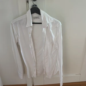 Vit skjorta från John Henric - Klassisk vit skjorta från John Henric med lång ärm och snygg krage. Skjortan har knappar framtill och är tillverkad i bomull, perfekt för en clean och stilren look.