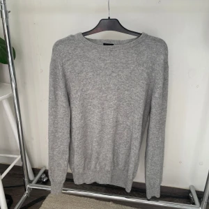 Ljusgrå merinoulltröja Swedish Fashion - Supermjuk och stilren ljusgrå tröja från Swedish Fashion i storlek L men sitter som en M. Tillverkad i 90% merinoull och 10% kashmir för en lyxig och skön känsla. Klassisk rund halsringning och långa ärmar, perfekt för lager-på-lager under kyliga dagar.