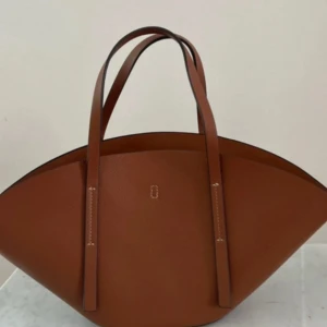 Brun axelväska i skinn Wide shopper gina tricot  - Ny kostar 399kr Säljer en brun axelväska i skinn med cool, bågformad design och långa handtag. Väskan har stilrena sömmar och minimalistisk look, perfekt för dig som gillar trendiga accessoarer med lite edge. Rymmer allt du behöver till vardags och mer därtill.