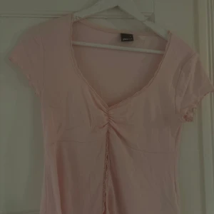 Ljusrosa topp med snörning från Gina Tricot - Supersöt ljusrosa topp från Gina Tricot med korta ärmar och v-ringning. Toppen har snygg snörningsdetalj framtill och spetskant längs urringningen💕💕