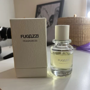 Fugazzi Vanilla Haze parfym - Fugazzi Vanilla Haze är en stilren parfym i en genomskinlig glasflaska med vit kork. Doften har en mjuk vaniljkaraktär och flaskan kommer i en elegant ljusbeige kartong. Perfekt för dig som gillar minimalistisk design och söta doftnoter.