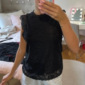 Svart spetsblus med volangärm - Supersöt svart blus från H&M i spets med fina volangärmar och rund halsringning. Blusen är ärmlös och har ett vackert spetsmönster över hela plagget samt en liten knapp i nacken. Nästan helt oanvänd💞💞