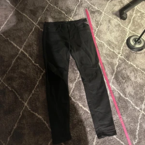 Svarta Replay jeans, storlek 31/30 - Svarta jeans från Replay med klassisk femficksdesign och diskret Replay-logga i rött vid fickan. Jeansen har en bra passform och är tillverkade i ett stretchigt bomullsmaterial som sitter snyggt längs benen. Perfekta för dig som gillar stilrena och bekväma jeans.