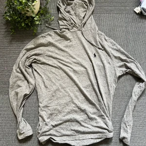 Grå hoodie från Polo Ralph Lauren - Snygg grå hoodie från Polo Ralph Lauren med klassisk broderad logga på bröstet. Tröjan har huva med snörning och är tillverkad i mjuk bomullsmix. Perfekt för en chill och avslappnad stil. Långärmad och i normal passform.