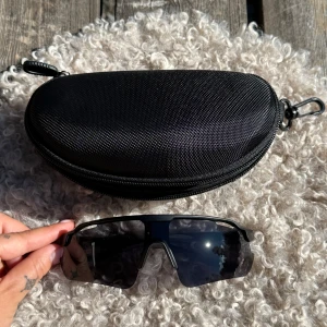 Svarta sportiga solglasögon Eyekønink - Säljer ett par svarta sportiga solglasögon från Eyekønink med breda, rektangulära linser och cool wraparound-design. Glasögonen har mattsvarta bågar i syntetmaterial och kommer med ett hårt svart fodral. Perfekta för dig som gillar en modern och aktiv stil. Säljer två par 500kr/st