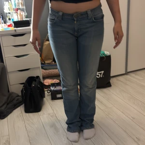 Blå strait jeans från Denim Birds - Säljer ett par ljusblå strait jeans från Denim Birds med snygga gula sömmar och broderade detaljer på bakfickorna. Klassisk femficksmodell med låg midja och raka ben. Perfekt för dig som gillar retrovibbar och vill ha en chill stil.