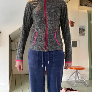 Grå sportkofta från H&M med rosa detaljer - Gråmelerad sportkofta från H&M Sport med lång ärm och snygga rosa detaljer vid dragkedja, fickor och muddar. Koftan har en slim passform och är tillverkad i mjukt syntetmaterial, perfekt för träning eller chill. Dragkedja framtill och två fickor med rosa kant. För liten för mig som ni kanske ser🤞 stor i storlek har haft den sedan jag gick i tvåan och nu börjar den bli för liten. Men skicket är fortfarande väldigt bra.