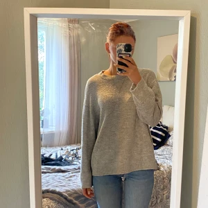 Grå stickad tröja i loose fit - Mysig grå stickad tröja med rund hals och avslappnad, loose passform. Perfekt för lager-på-lager och enkel att styla med jeans eller kjol. Långärmad och ribbade muddar vid ärmslut och nederkant. Enkel och stilren design som funkar året runt.
