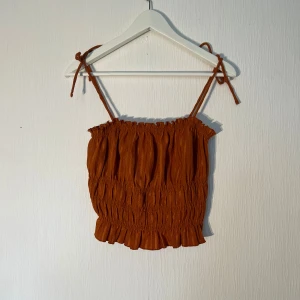 Rostbrun smockad linnetopp H&M S - Superfin rostbrun linnetopp från H&M i storlek S med smockad struktur och volangkant nertill. Axelbanden är tunna och knyts på axlarna. Använd få gånger! 