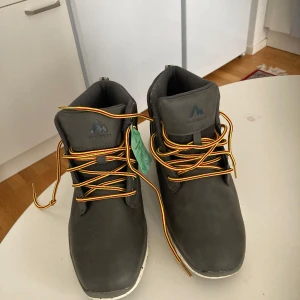 Grå kängor från McKinley strl 40 - Snygga grå kängor från McKinley med vattentätt Aquamax-membran och andasfunktion. Skorna har gula och röda snören, robust platt sula och är perfekta för utomhusaktiviteter. Tillverkade i syntetmaterial och mocka-look. Modell: Richard AQX.