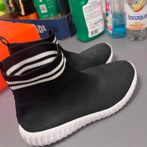 Svarta sock-sneakers med vita ränder - Svarta sneakers i stickad modell med högt skaft och vita ränder upptill. Skorna har en vit, räfflad sula och är gjorda i ett stretchigt syntetmaterial som sitter tajt runt foten. Perfekta för en sportig och trendig look. Mycket lätta och jättesköna skor! Perfekt för inneskor i skolan tex