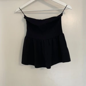Svart volangig linnetopp - Snygg svart linnetopp med  och volangig nederdel. Toppen har en enkel och stilren design som passar perfekt till jeans eller kjol. Materialet känns mjukt och lätt, perfekt för varmare dagar.