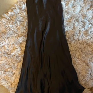 Svart satinkjol från Gina Tricot - Supersnygg lång svart satinkjol från Gina Tricot i storlek 34. Kjolen har en glansig finish och en mjuk, följsam passform som ger en elegant siluett.