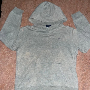 Grå hoodie från Polo Ralph Lauren XL - Säljer en klassisk grå hoodie från Polo Ralph Lauren i storlek XL. Tröjan har huva, magficka och den ikoniska lilla broderade loggan på bröstet. Perfekt för chill dagar och enkel att matcha med jeans eller joggers. (OBS! hoodien har missfärgningar på vissa ställen)