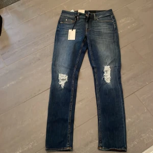 Tiger of Sweden blå jeans W28 L32 - Snygga blå jeans från Tiger of Sweden med låg midja och raka ben. Jeansen har slitna detaljer på knäna och klassiska fem fickor. Materialet är jeans med orange kontrastsömmar för en cool look.kontakta för info 