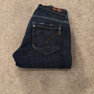 Dondup jeans George  - Snygga mörkblå jeans med raka ben och coola orange sömmar på bakfickorna. Klassisk femficksmodell med en mörk tvätt och diskreta slitningar. Jeansen har en normal passform och är perfekta för dig som gillar en stilren look.