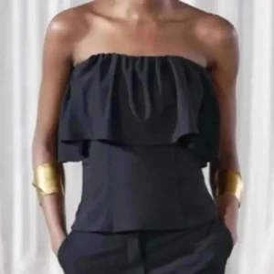 Svart bandeau tubtopp med volang - Snygg svart bandeau tubtopp med bred volang upptill som ger en trendig och luftig look. Toppen är axelbandslös och är sååå snygg!! Inga defekter alls