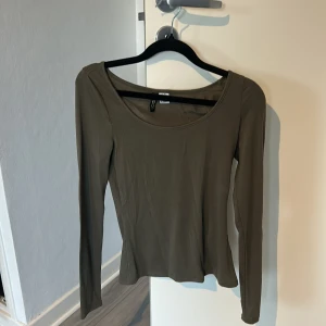 Olivgrön långärmad topp H&M - En stilren olivgrön långärmad topp från H&M med rundad, djup urringning. Tunn och mjuk i bomullsmix, perfekt att styla med jeans eller kjol. Enkel design som funkar till många looks.