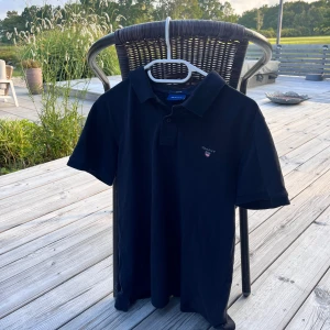 Svart pikétröja från GANT - Svart pikétröja från GANT med klassisk krage och korta ärmar. Tröjan har en liten broderad logga på bröstet och knäppning vid halsen. Tillverkad i mjuk bomull som känns skön mot huden. Perfekt för en clean och stilren look. Fin fin piké men lite för liten för mig storlek M. Säljer för 199kr😊 priset kan diskuteras 