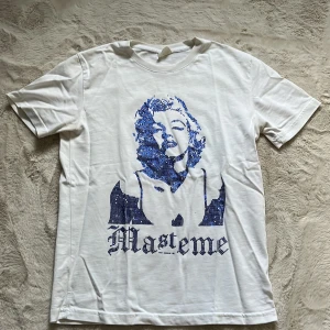 Vit t-shirt från Mastemé med tryck - Vit t-shirt från Mastemé med blått tryck av ikonisk person och text på framsidan. Klassisk passform med rund hals och korta ärmar. Perfekt för dig som gillar streetstyle och coola prints.