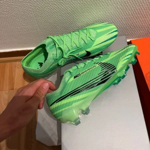 Gröna Nike fotbollsskor med snörning - Snygga fotbollsskor från Nike i en fräsch grön färg med svarta detaljer och snörning. Skorna har en lätt och smidig syntetöverdel samt mönstrad sula för bra grepp på planen. Perfekta för dig som vill sticka ut på matchen.