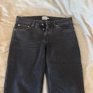 Svarta raka jeans från 157 - Svarta jeans från 157 med klassisk femficksdesign och raka ben. Jeansen har lägre midja och knäppning med knappar framtill. Materialet är robust denim i bomull och färgen är en snygg, något ”urtvättad” svart ton. Använda 2 gånger😍🤗