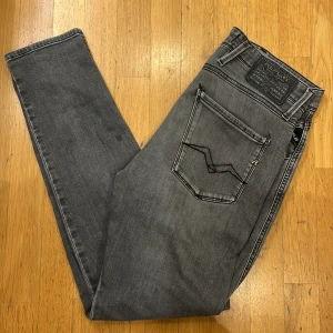 Replay Anbass grå slim jeans - Snygga grå jeans från Replay, modell Anbass med slim fit. Jeansen har klassisk femficksdesign, svarta detaljer och diskret Replay-logga på fickan. Materialet är mjukt och stretchigt jeans, perfekt för en modern och clean look. 