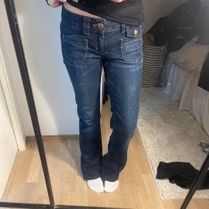 Mörkblå bootcut jeans från ONLY - Snygga mörkblå jeans från ONLY med bootcut-modell och coola fickdetaljer framtill. Jeansen har låg midja, klassiska guldiga knappar och är tillverkade i stretchig bomullsdenim för skön passform.