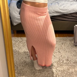 Lång kjol - Superfin rosa långkjol i stickat material med breda ribbor och en snygg slits på sidan. Kjolen har elastisk midja. Kjolen är helt ny och har inte används någon gång.