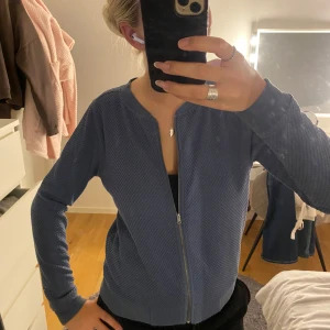 Blå kofta från Jacqueline de Yong - Säljer en blå kofta från Jacqueline de Yong i storlek S. Koftan har ett diskret strukturerat mönster, dragkedja framtill och ribbade muddar vid ärmslut och nederkant. Perfekt för lager-på-lager och enkel att matcha med olika outfits.