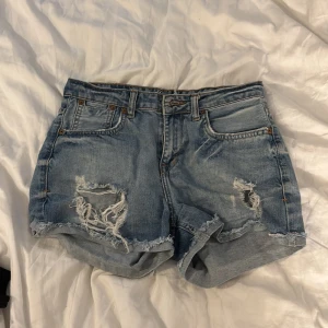 Blå jeansshorts med slitningar - Snygga blå jeansshorts från Project Jeans med råa kanter och slitna detaljer både fram och bak. Klassisk femficksmodell med knapp och dragkedja. Perfekt för dig som gillar en avslappnad och trendig stil.