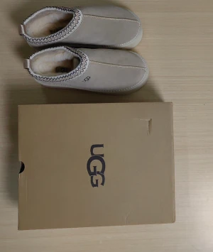 Beige UGG boots med fårull - UGG boots i beige mocka med mjukt fårullsfoder och vit platt sula. Skorna har dekorativt mönstrad kant upptill och praktisk hälflik för enkel påtagning. Perfekta för kalla dagar och riktigt mysiga att ha på sig.