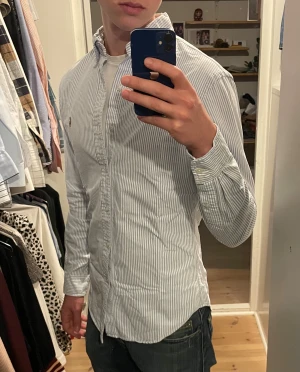 Randig skjorta från Ralph Lauren - Snygg vit och ljusblå randig skjorta från Ralph Lauren. Perfekt för dig som gillar stilrena och tidlösa plagg.