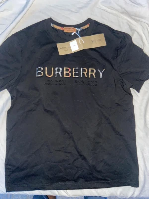Svart Burberry t-shirt med logga - Snygg svart t-shirt från Burberry med klassisk logga broderad på bröstet och texten 'London England' under. Rund hals och korta ärmar, tillverkad i mjuk bomull. Perfekt för dig som gillar stilrena designer med lyxig känsla.