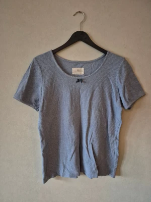 Blå ribbad topp med rosett - Supersöt ljusblå ribbad topp från Green Meadow med korta ärmar och liten rosett vid urringningen. Toppen har en rund halsringning och är i mjuk bomull, perfekt för en chill och stilren look.