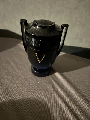 Mörk och stilren parfymflaska - Snygg och modern parfymflaska från Paco Rabanne, med en cool pokaldesign och ett stort V på framsidan. Perfekt för dig som vill sticka ut med din stil. Volym och ingredienser syns inte på bilderna.