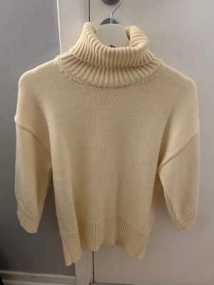 Gul stickad polotröja - Säljer en gul stickad polotröja med bred ribbad krage och muddar. Tröjan har en loose passform och är perfekt för kyliga dagar. Den höga polokragen ger en snygg och mysig look.