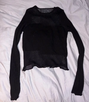 Svart ribbad topp - Svart långärmad topp från ASOS med ribbad struktur och lätt transparenta partier. Tröjan har en rund halsringning och vågig kant nedtill som ger en snygg detalj. Perfekt att styla med jeans eller kjol för en cool look. Liten i storlek