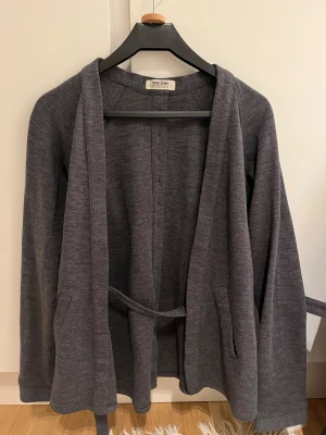 Grå kofta med bälte från Acne Jeans - Snygg mörkgrå kofta från Acne Jeans med bälte i midjan och knappar längs ryggen funkar bra under vintern 