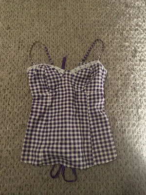 Lila rutig korsett-topp med snörning - Superfin korsett-topp med lila och vitt rutigt mönster, smala axelband och spetsdetalj upptill.  Kommer inte till någon användning!