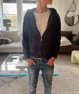 Svart Raphl Lauren hoodie - Säljer en svart Raphl Lauren hoodie med rött Raphl Lauren märke på vänster bröst. Det kanske inte syns på bilden men hoodien har blivit ganska sliten då den har tappat lite sin svarta färg och har några hål i sig, men de tär inget man märker till. Det är bara att slå en pling 🛎️ kring några funderingar