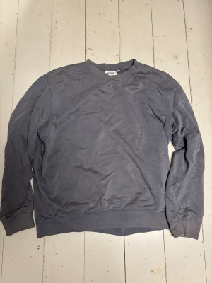 Grå sweatshirt från Weekday - En enkel och stilren grå sweatshirt från Weekday med rund hals och ribbade muddar vid ärmslut och nederkant. Tröjan har en loose passform och är tillverkad i mjuk bomull, perfekt för chill dagar. Passar dig som gillar minimalistisk stil. Den är lite solblekt runt kragen och i ärmarna. 