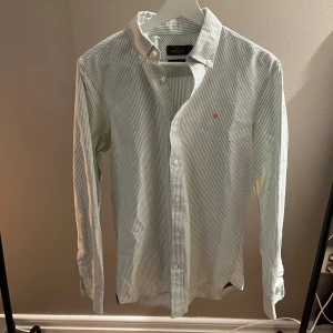Morris Skjorta - Tja! Säljer en riktigt snygg randig Morris skjorta. Den är i  bra skick 7/10. Den har täcken på användning som visas på sista bilden men är fin overall skick. Skjortan är i färgen vit och blå. Märket är orange. Storlek S kan passa M. Den är perfekt till alla tillfällen men speciellt våren och sommaren☀️ Nypris runt 1800 kr Hör av dig vid funderingar🙌