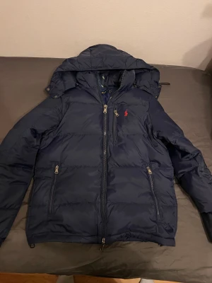 Mörkblå dunjacka från Polo Ralph Lauren - Säljer en mörkblå Polo Ralph Lauren jacka med luva, dragkedja framtill och två sidofickor med dragkedja. Perfekt för kalla dagar och riktigt snygg passform. Storlek S. Skriv ifall ni undrar nått. Pris går att diskuteras 