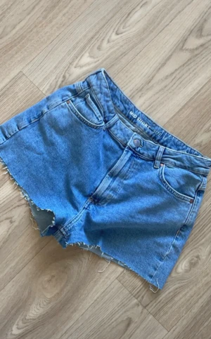 Blå jeansshorts från Never Denim - Snygga blå jeansshorts från Never Denim med rå kant och klassisk femficksdesign. Shortsen har knapp och dragkedja framtill samt stora bakfickor. 🥰